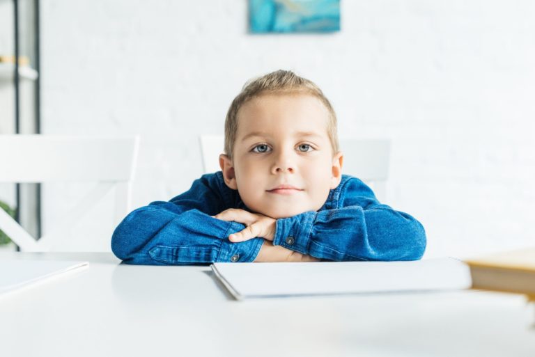 Rozkošné malé dítě sedí u stolu s prázdnou notebook a při pohledu na fotoaparát - null